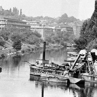 Riverfront view featuring a large building and docked boats.