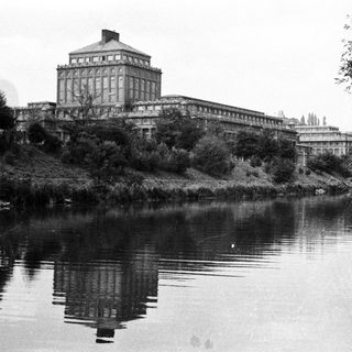 Grand building reflected in water, surrounded by greenery.