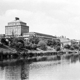 Large building overlooks a river, reflected in the water.