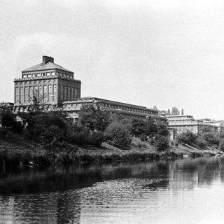 Large building overlooks a river with foliage and trees.