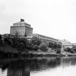 Large building overlooking a river with visible vegetation.