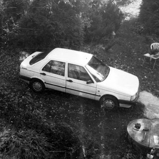 Car sits in overgrown yard with furniture.
