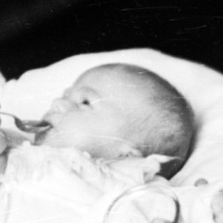 Woman holding a baby, likely a newborn, in a vintage setting.