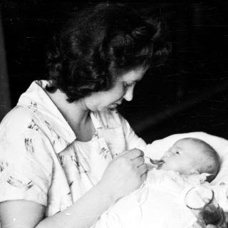 Woman holding a baby, likely a newborn, in a vintage setting.