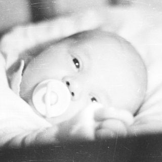 Here's a brief summary of the image: Baby lying in a crib, holding a pacifier.