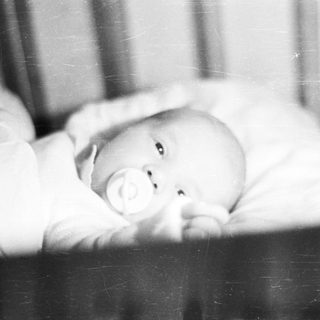 Here's a brief summary of the image: Baby lying in a crib, holding a pacifier.