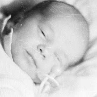 Here's a brief summary of the image: Black and white photo of a baby lying down.