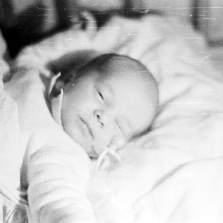 Here's a brief summary of the image: Black and white photo of a baby lying down.