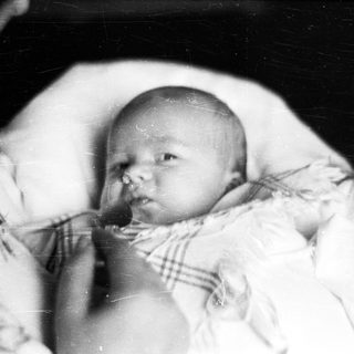 Black and white photo depicts a baby in vintage clothing.