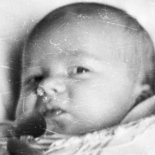 Black and white photo depicts a baby in vintage clothing.