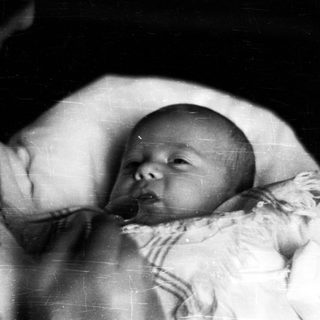 Here's a brief summary of the image: Black and white photo of a baby in a crib.