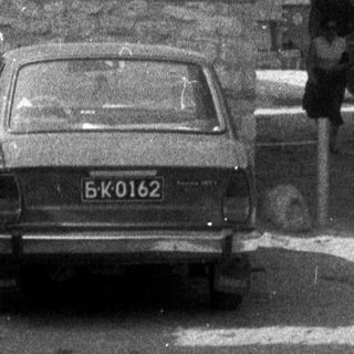 Black and white image of a street with people and a car.