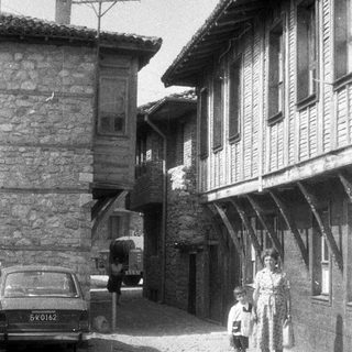 Black and white image of a street with people and a car.