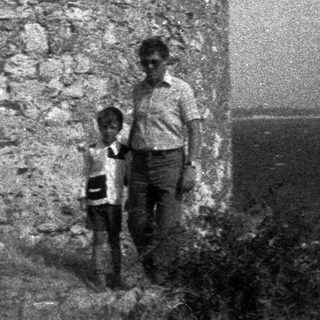 Two children standing near a stone wall by the water.