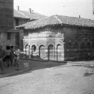 Historic stone building with arched facade and people nearby.