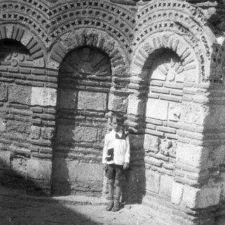 Boy stands beneath arched doorway in old stone building.