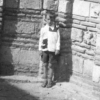 Boy stands beneath arched doorway in old stone building.