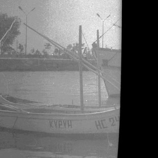Boat on water, with trees and lights in background.