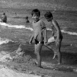Two boys walking on a beach with people in background.