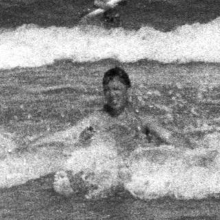 People swimming in a wavy ocean, monochrome photograph.