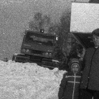 Two people stand in deep snow near a building.