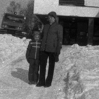 Two people stand in deep snow near a building.