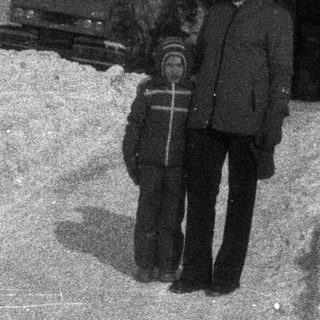 Two people stand in deep snow near a building.