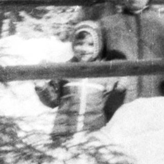 Man standing in snowy woods near a tree.