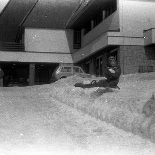 Man walking past a building with snow piled high.
