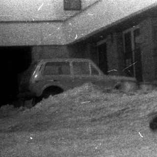 Child sledding down a snowy hill with a building nearby.