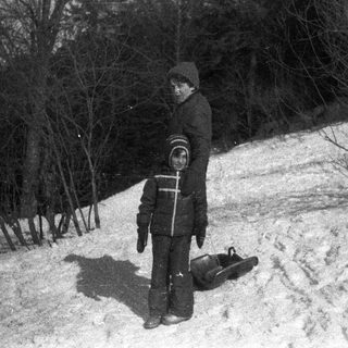 Boy stands on snowy hill with a sled.