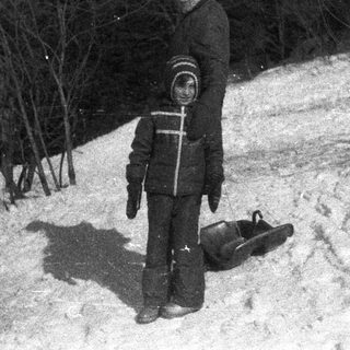 Boy stands on snowy hill with a sled.