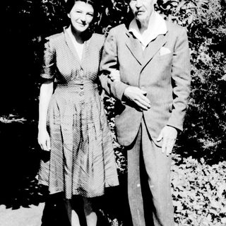 Here's a brief summary of the image: A man and woman stand together in a garden setting.