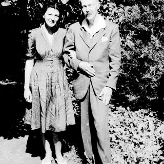 Here's a brief summary of the image: A man and woman stand together in a garden setting.