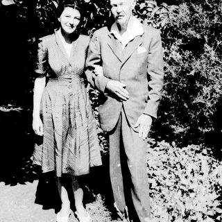 Here's a brief summary of the image: A man and woman stand together in a garden setting.