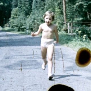 Child runs down a road through a forested area.