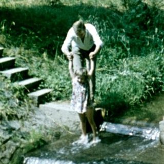 Woman stands near a small waterfall in a wooded area.