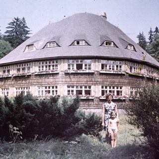 Woman and child stand before unusual, round wooden building.