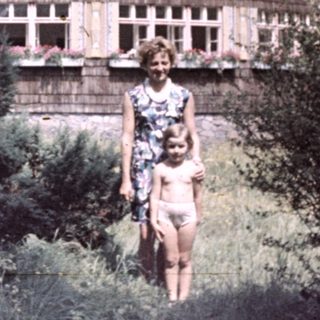 Woman and child stand before unusual, round wooden building.
