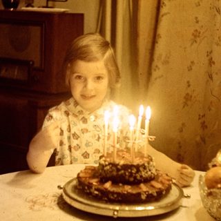 Child sits at a table with a birthday cake.