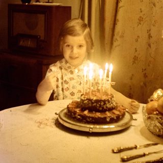 Child sits at a table with a birthday cake.