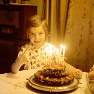 Child sits at a table with a birthday cake.