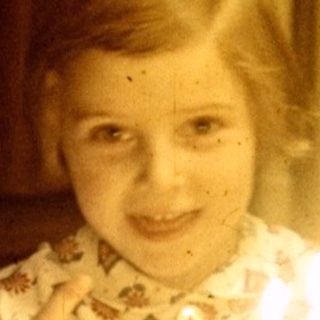 Child sits at a table with a birthday cake.