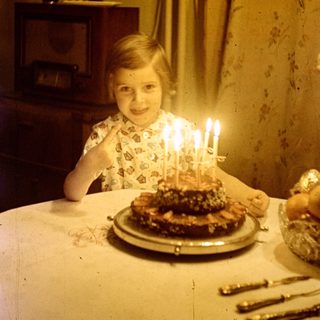 Child sits at a table with a birthday cake.
