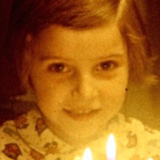 Child sits at a table with a birthday cake.