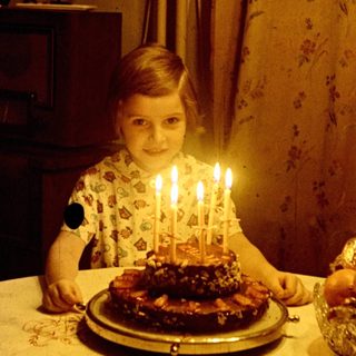Child sits at a table with a birthday cake.