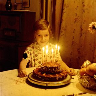 Child sits at a table with a birthday cake.