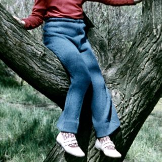 Girl playfully sits on a tree branch outdoors.