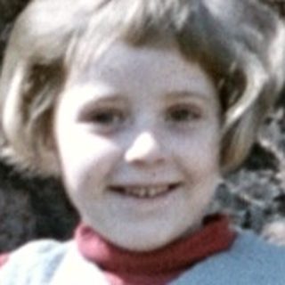 Girl stands near rocks, holding a flower.