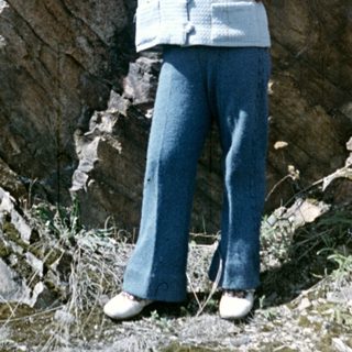 Girl stands near rocks, holding a flower.
